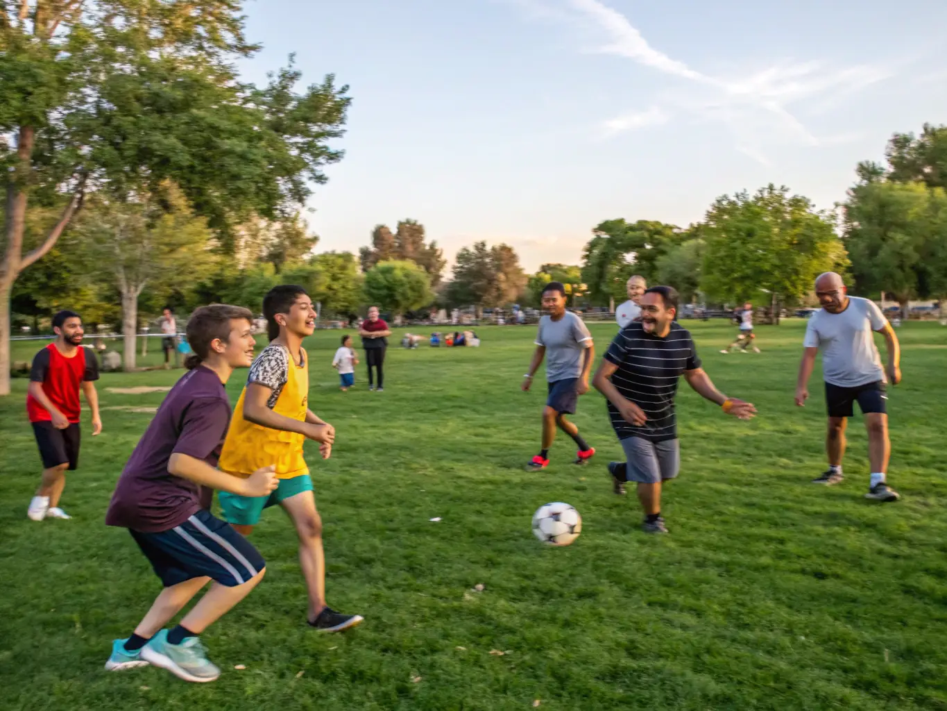 A lively scene of employees and their families participating in a recreational sports day, featuring activities like volleyball, soccer, and relay races in a park.